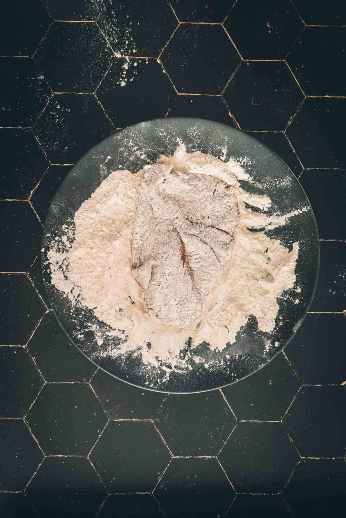 Floured cutlet on a plate on a black background.