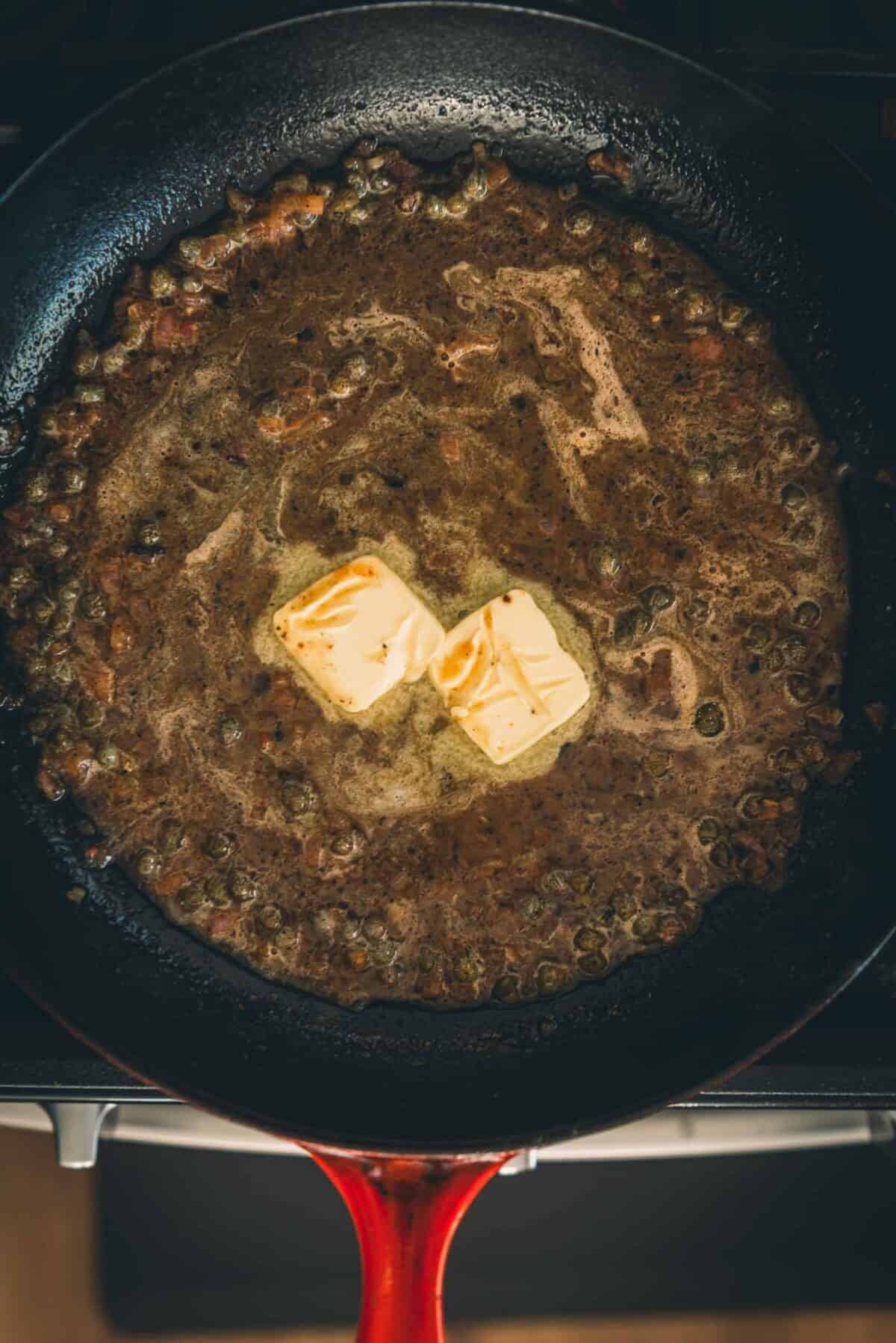 A frying pan with butter and capers.