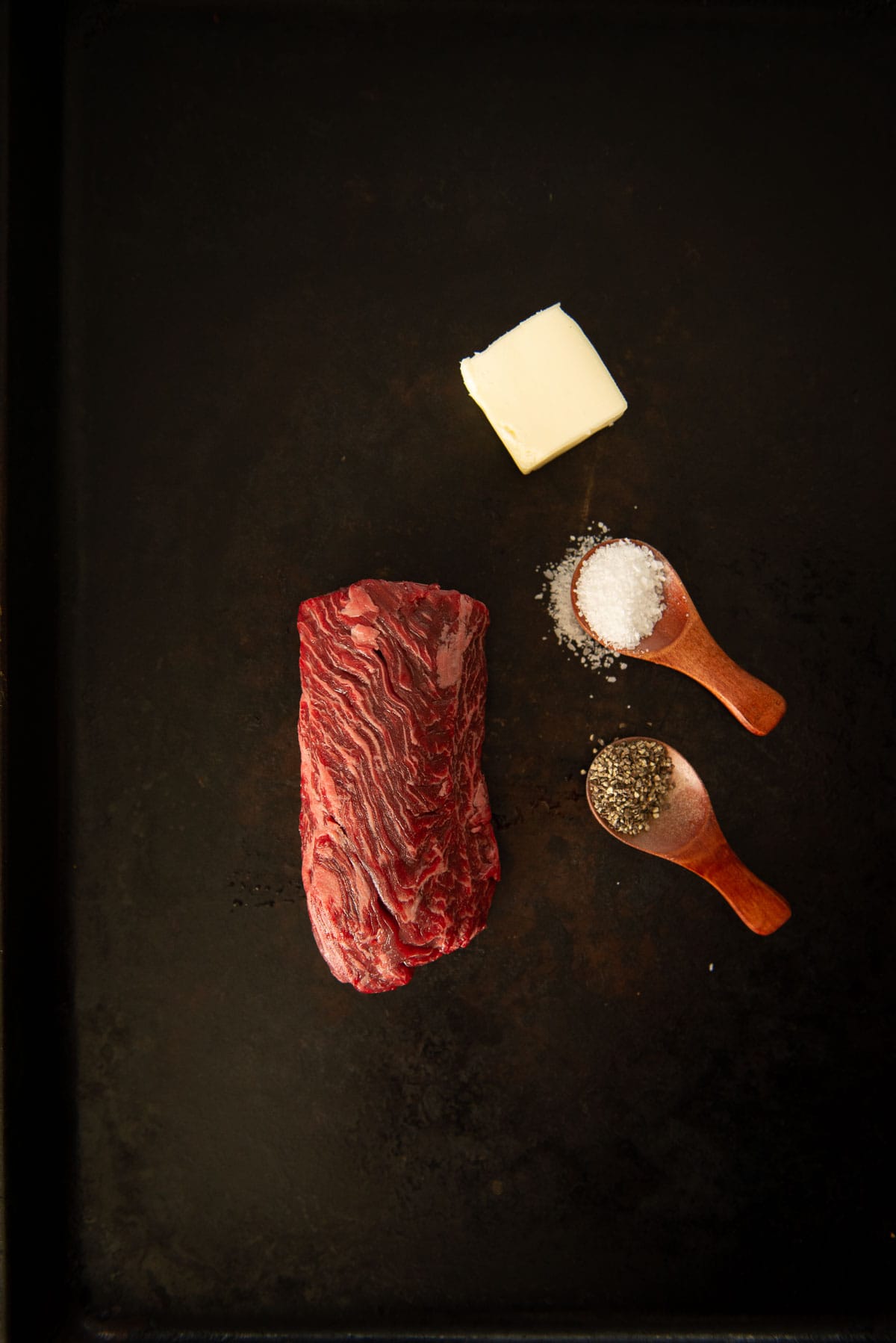 A hanger steak with salt and pepper on a black tray.