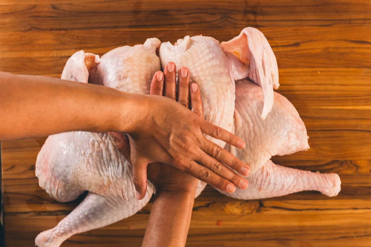 Hands pressing spatchcock turkey flat.