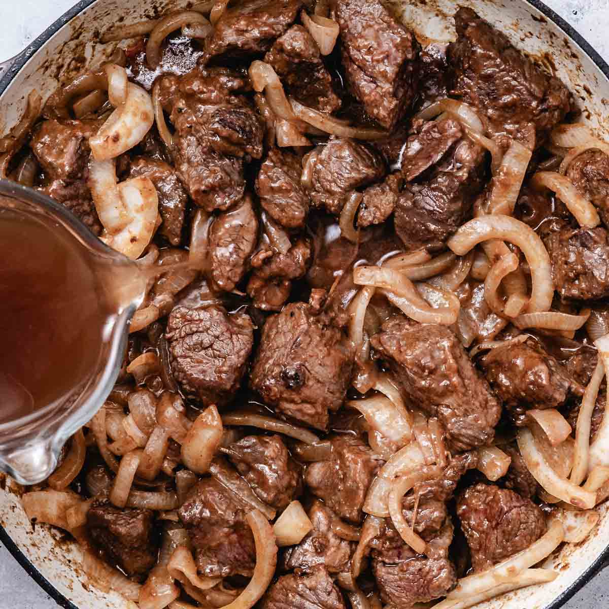 Beef broth being added to browned beef and onions
