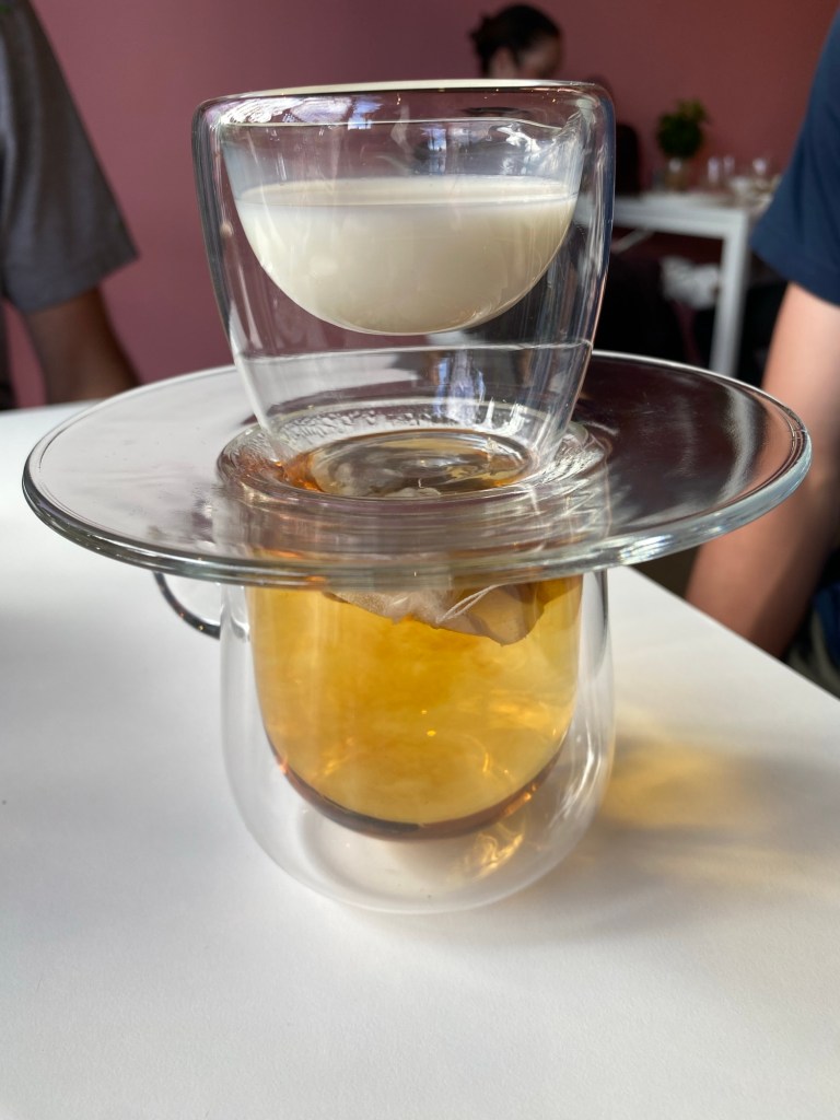 A cup of brewing tea in an double walled glass cup/mug. Sitting on top is a glass saucer and on top of that is a jug of milk, which is also double walled glass. I can't imagine if you can make sense of this but it looks pretty cool