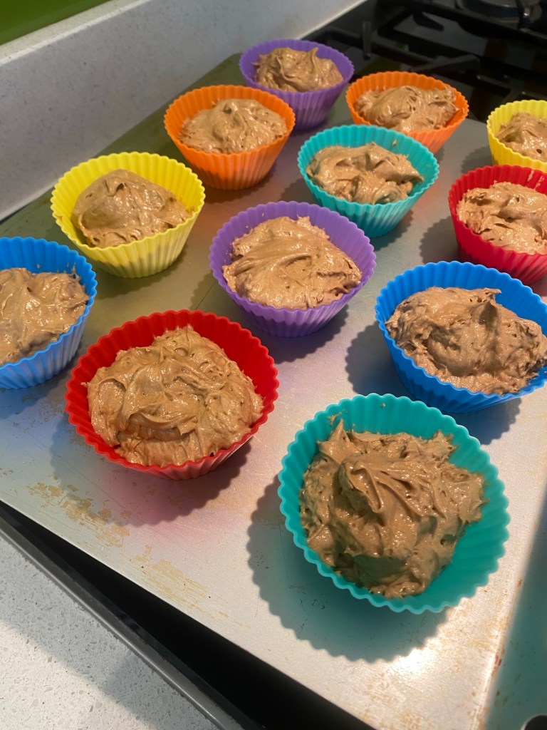 Twelve filled cupcake cases sitting on an aluminium tray, ready to go in the oven