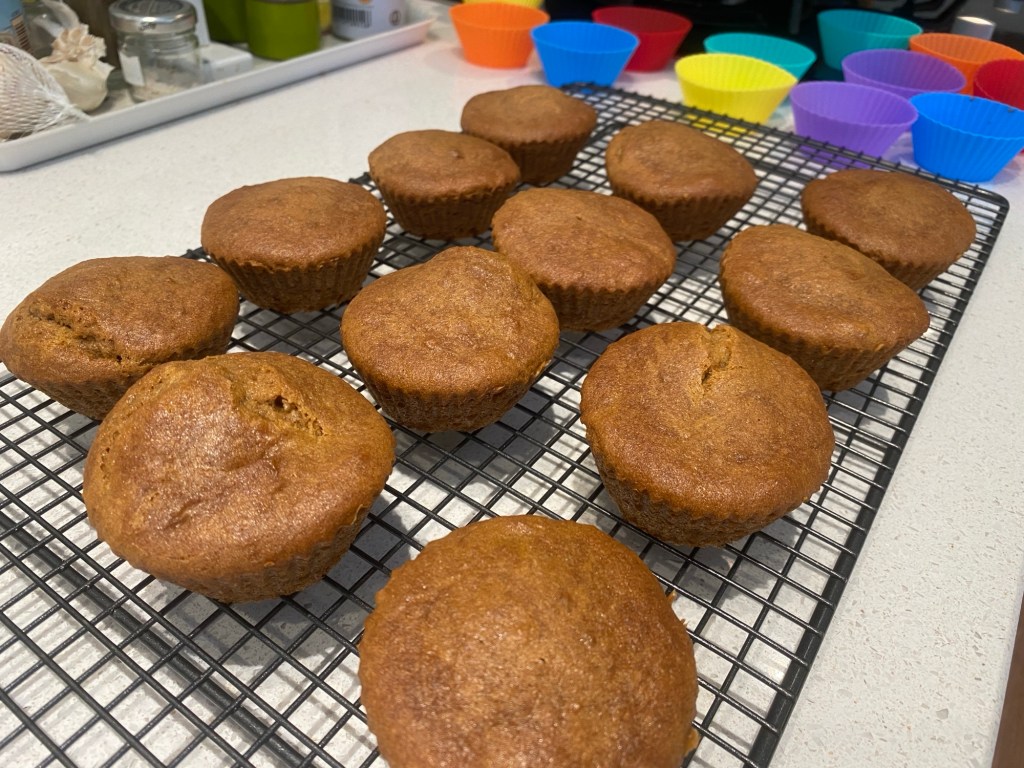 a wire cooling rack with twelve brown (coffee) cupcakes that have recently been removed from their silicon cases, which are in view at the back