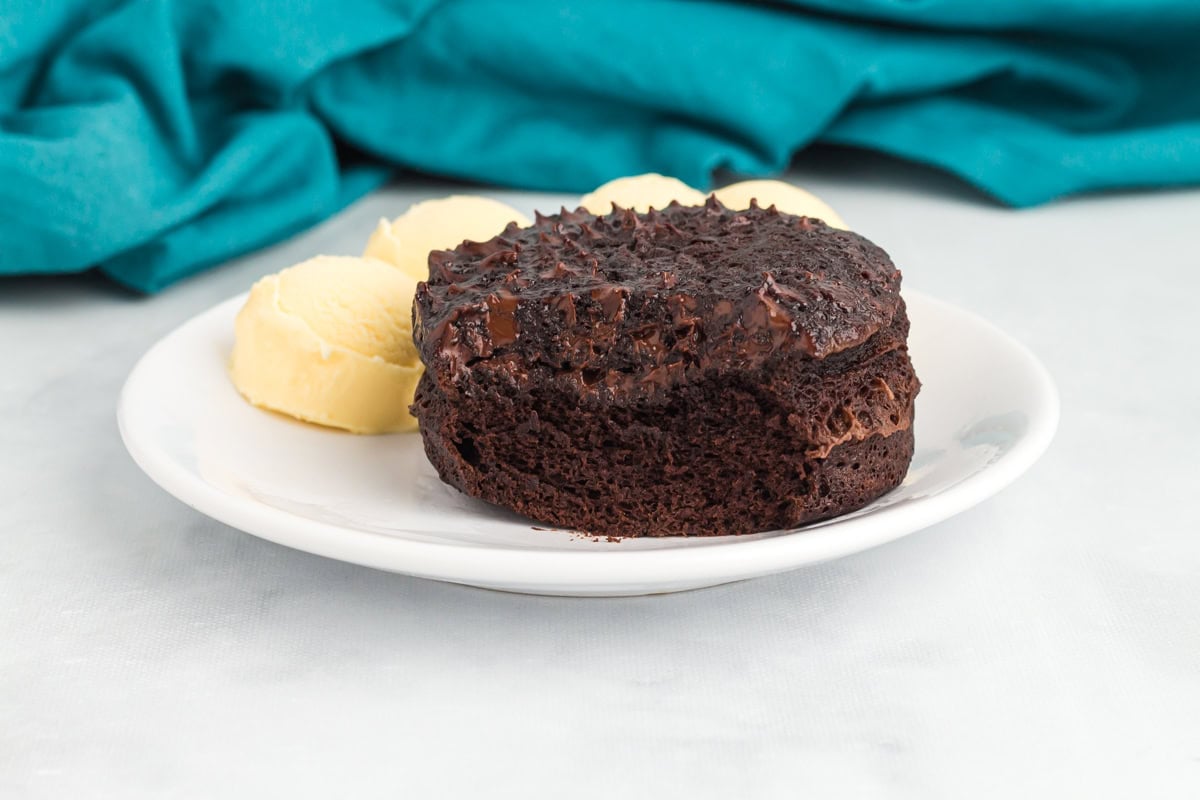 Flourless mug cake turned out onto a plate and served with scoops of vanilla ice cream