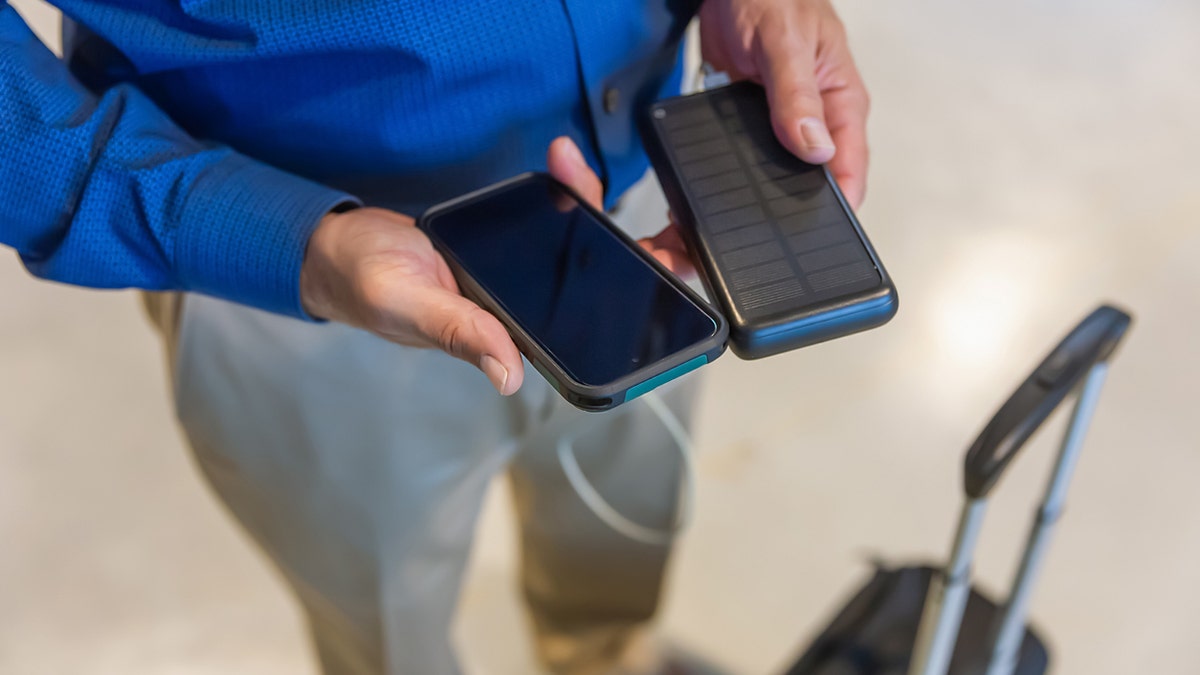 A person holds a phone with a portable charger.