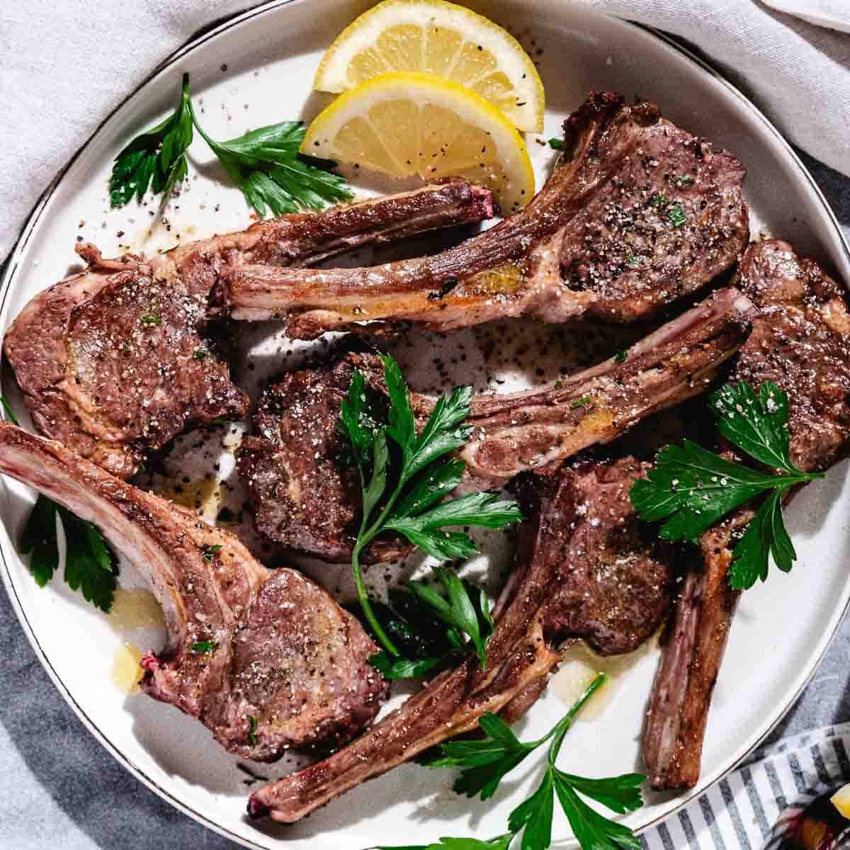 baby lambchops with lemon slices on white plate.