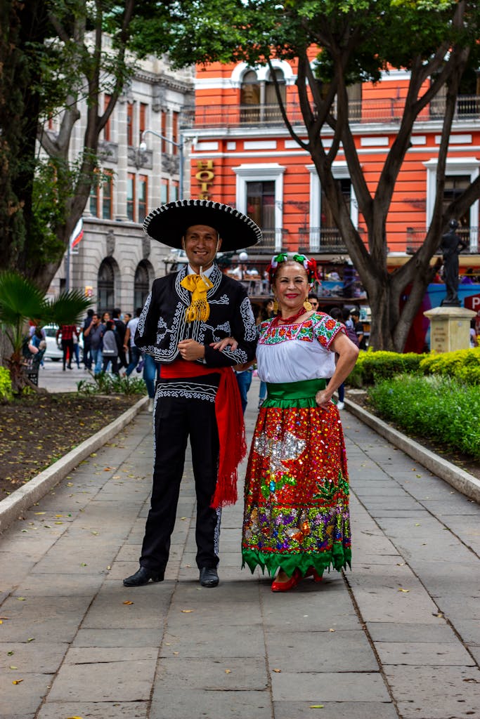 Man and woman dressed in traditional Mexican outfits in a vibrant Puebla street scene.