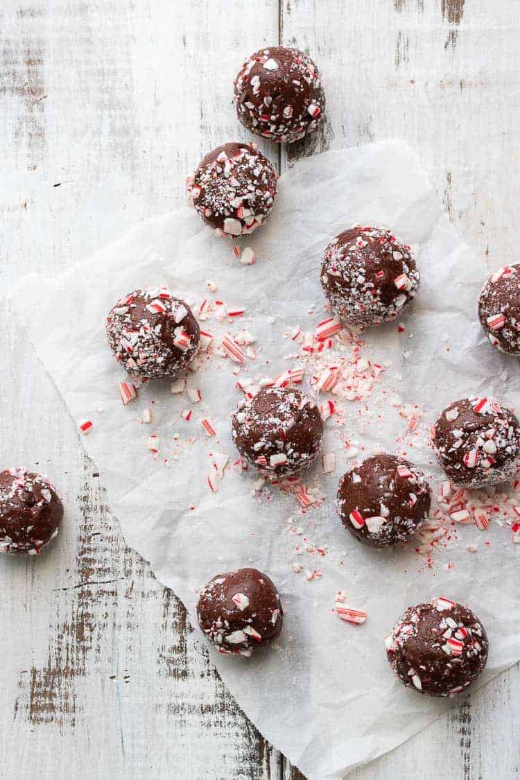 A festive vegan holiday treat made in only 5 minutes! These no bake chocolate peppermint balls even have a trick to keeping them whole food and healthy. #vegandessertrecipes #veganchristmas Brownie balls covered in crushed candy cane spread out on a white wooden table