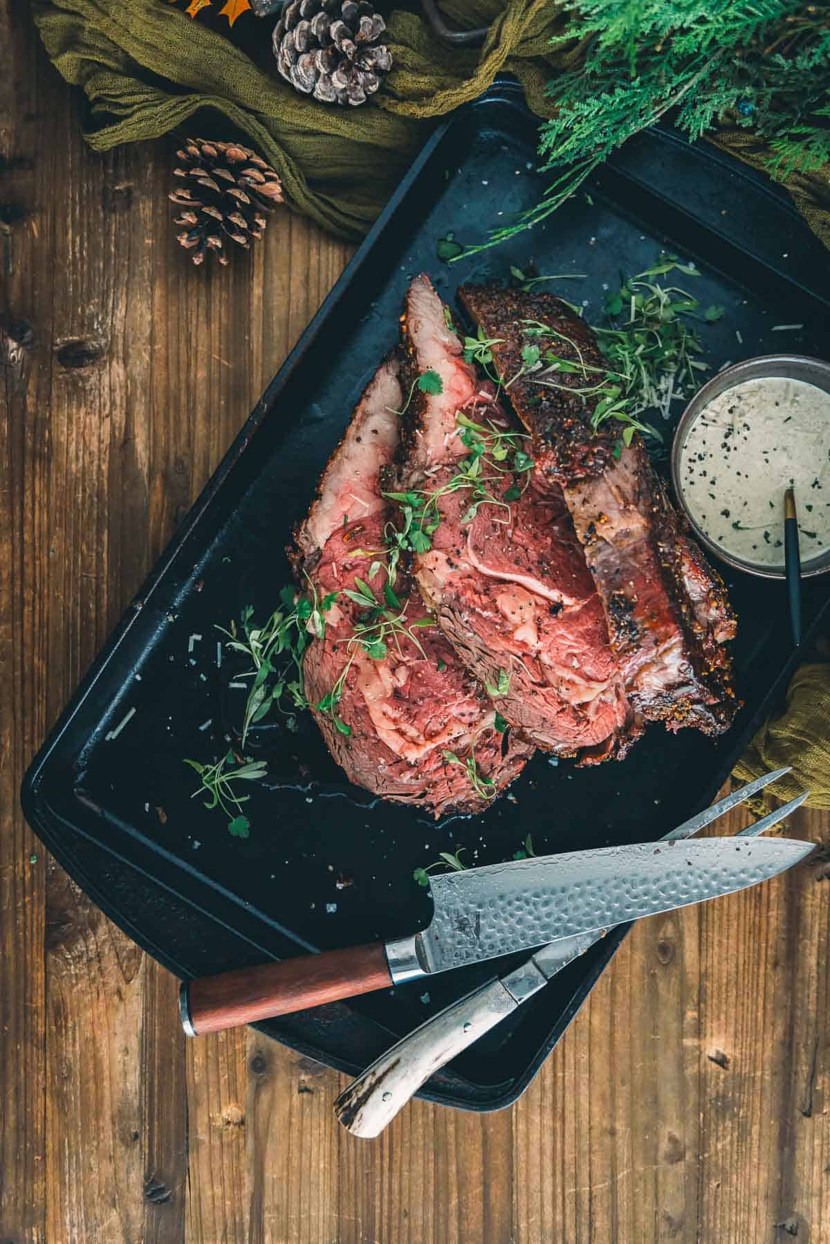 A reverse sear prime rib roast, sliced, on a tray for serving with a sauce on it.