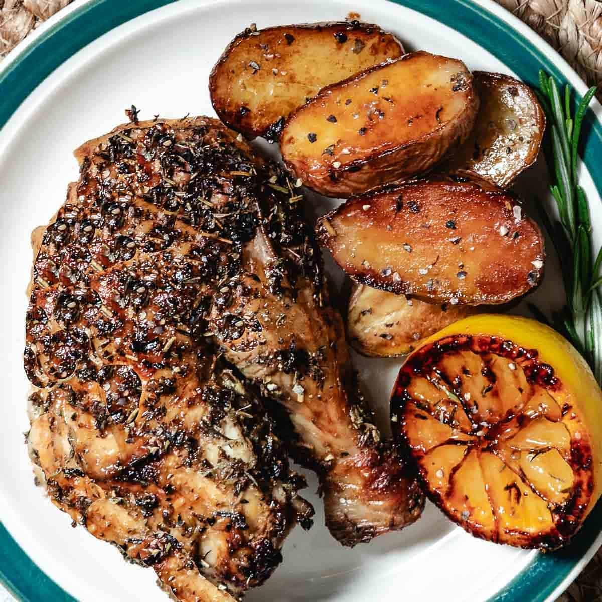 Roasted chicken leg quarter with crispy potatoes and charred lemon on a plate