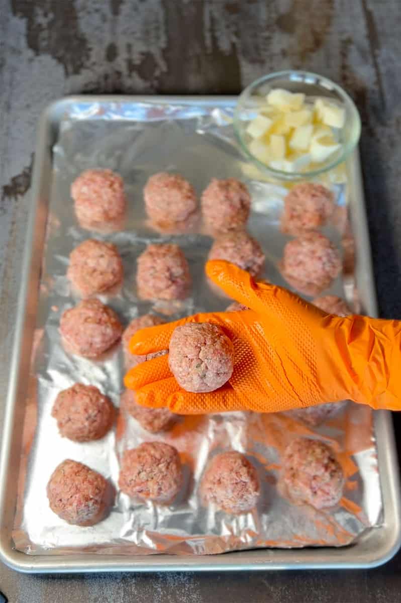 hand with orange glove showing raw meatball.