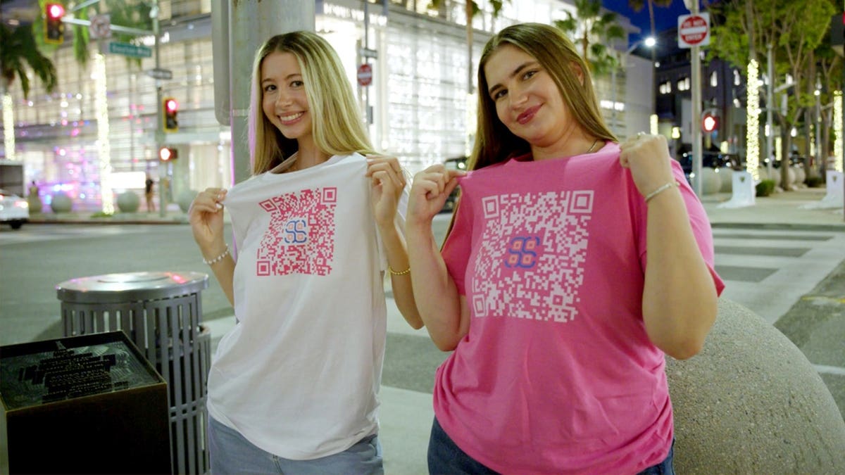 Two girls show shirts with QR codes on the front.