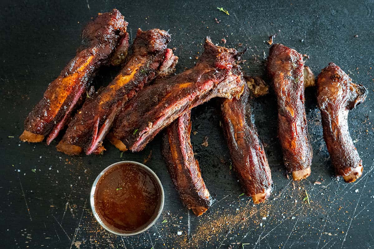 sliced smoked beef back ribs on black platter with sauce.