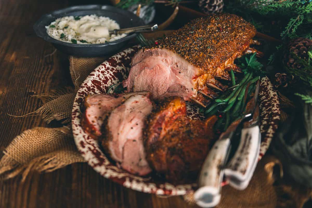 Smoked rack of pork on a platter with rosemary and veggies.