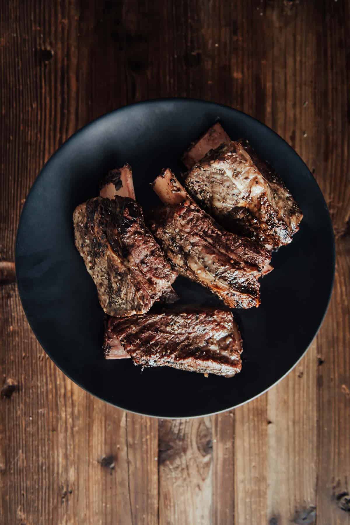 Beef ribs on a black plate on a wooden table.