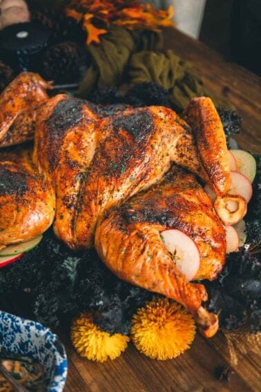 Roasted spatchcock turkey trimmed with apple slices on a serving platter over kale.