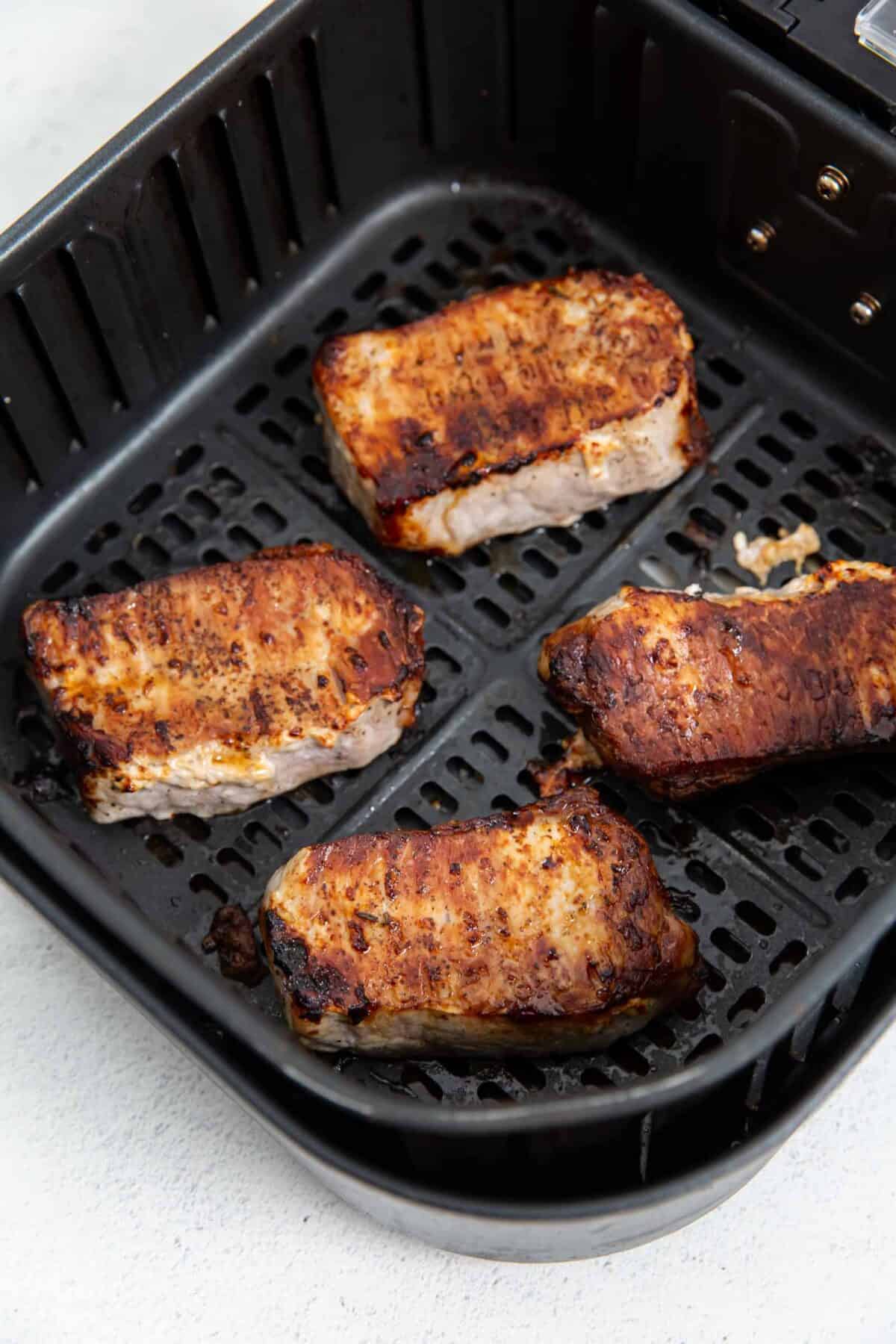 Golden brown exterior of pork chops in an air fryer basket.