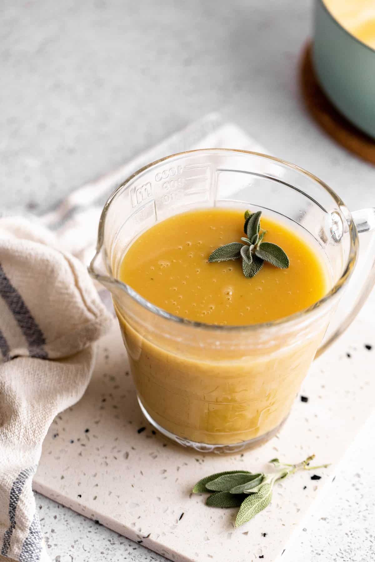 Cup filled with thick gravy garnished with sage.