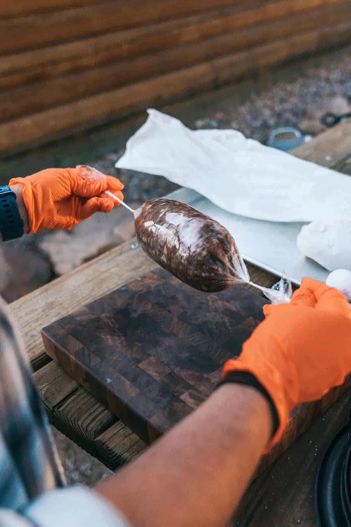 two hands pulling on ends of plastic wrap-wrapped sausage.