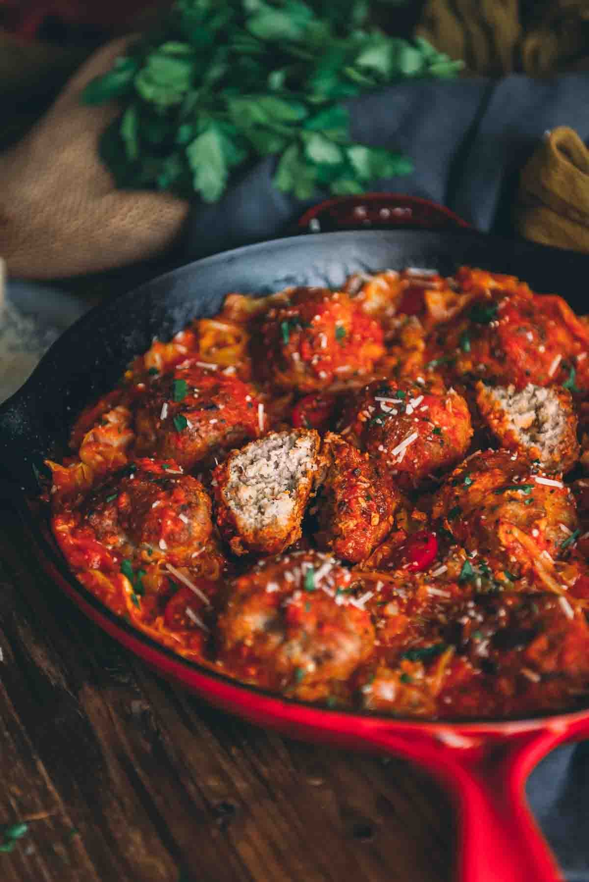 Showing one meatball cut open in a platter of marinara coated ones.